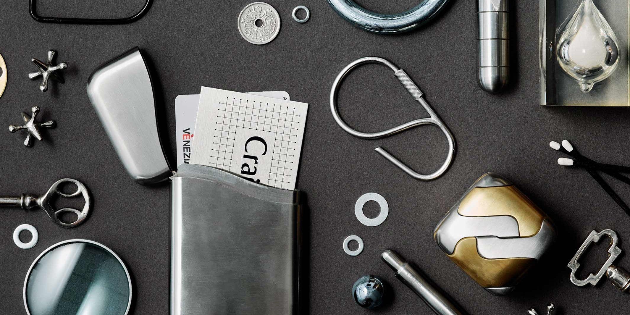 Everyday Carry Kollektion von Craighill: Karten-Etui aus Edelstahl, Schlüsselring, Taschenmesser und Metall-Objekte auf dunklem Grund